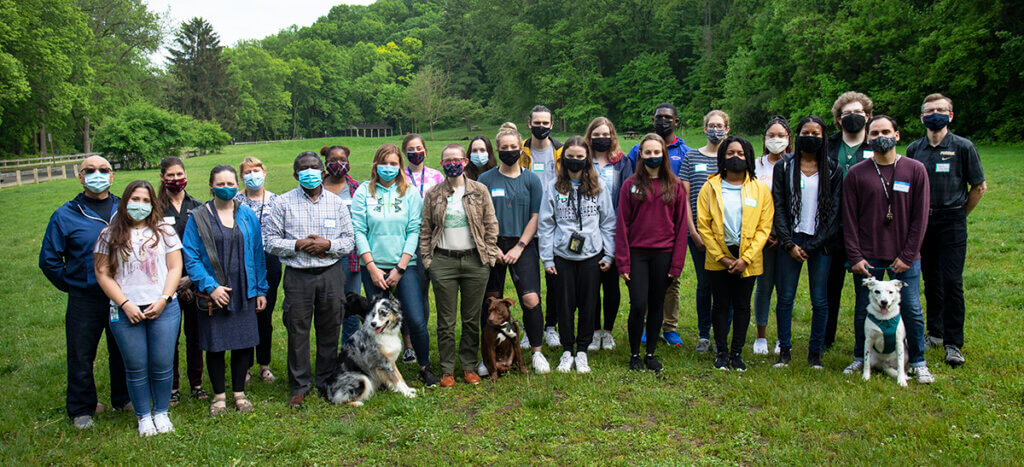 veterinary scholars and some faculty members along with some pets gather for a group photo while wearing masks outside against a lush green backdrop of the park