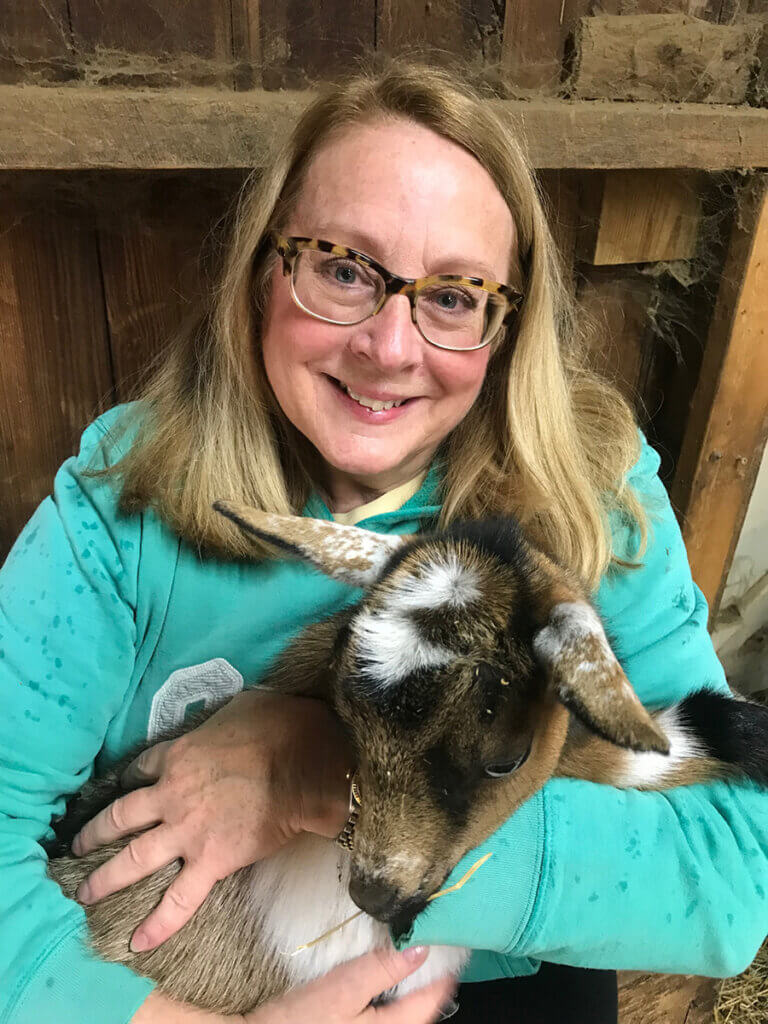 Joy smiles holding a goat in a barn