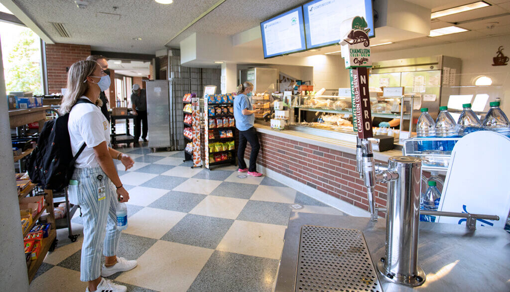 the cold brew tap is pictured in the cafe with nearby students standing by looking at the menu screens