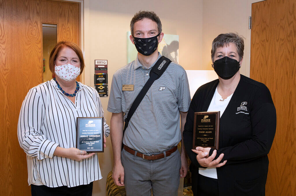 Shelly, Bryan, and Paige stand together smiling behind face masks as Shelly and Paige hold up their plaques