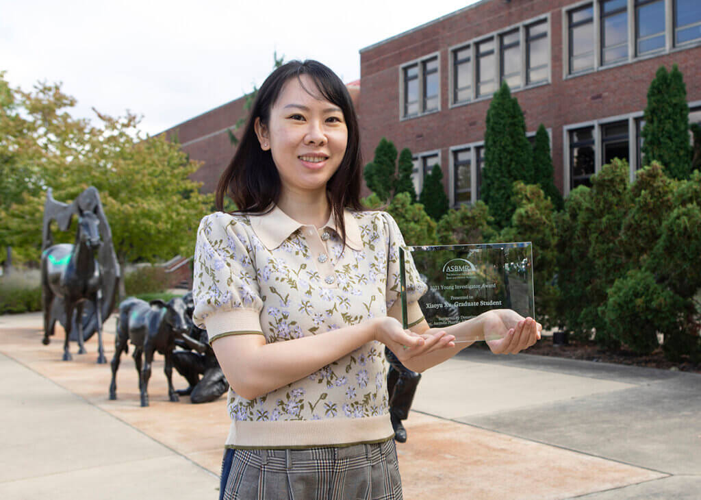 Xiaoyu stands in front of the Continuum sculpture outside of Lynn Hall holding up her award