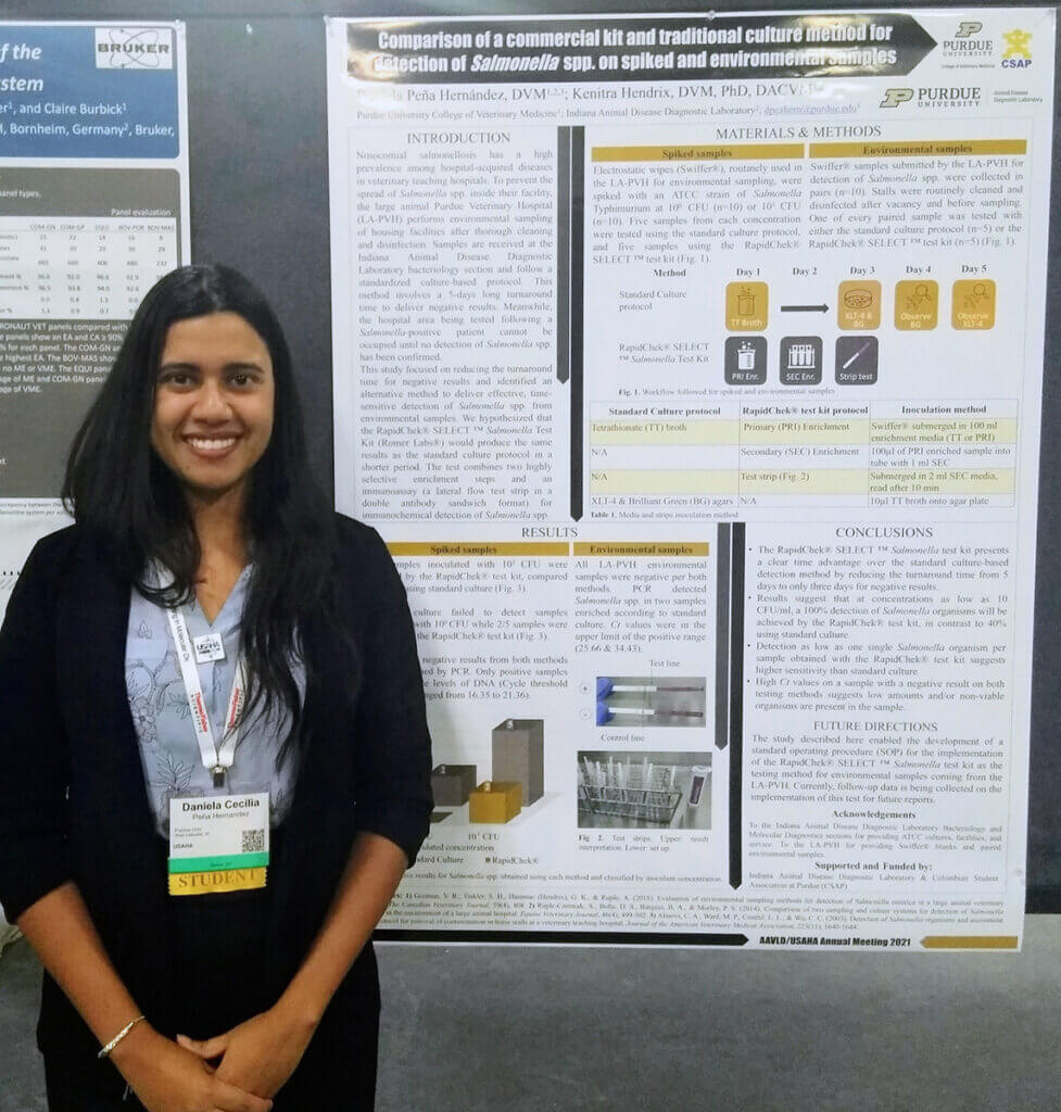 Daniela smiles standing beside her research poster