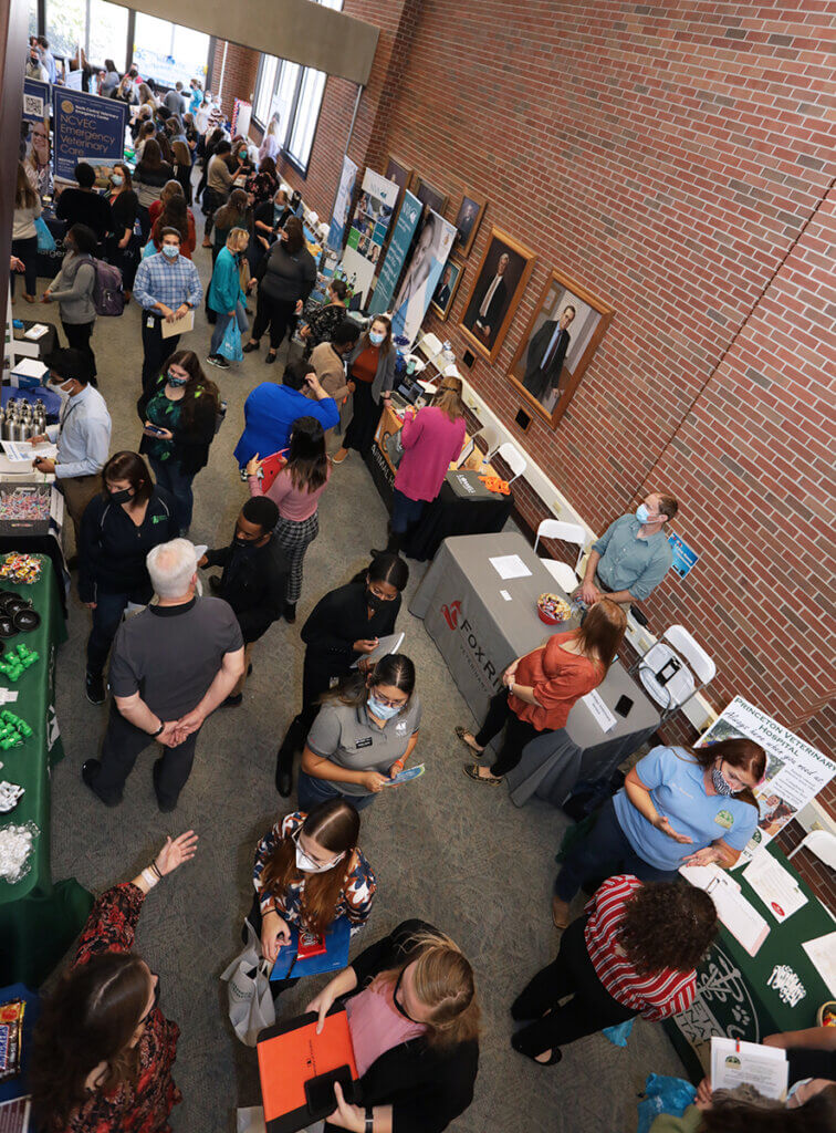 A crowd of students walks between vendor booths lining the walls of the library