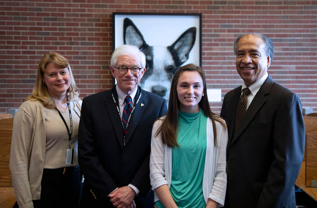Dr. Salisbury, David Williams, Dr. Katie Sands, and Dean Willie Reed stand in front of Dr. Sands artwork displayed in the library