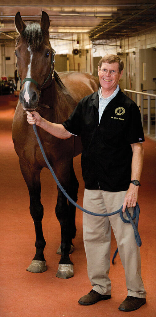 Dr. Adams stands in the Purdue University Large Animal Hospital next to a horse holding it's harness