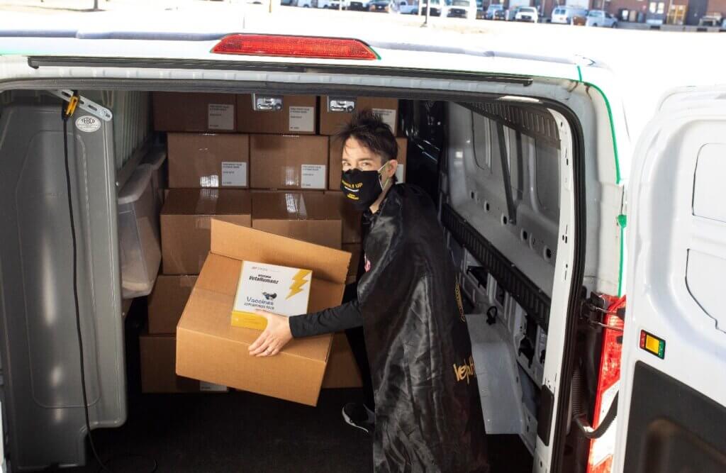 Sporting a League of VetaHumanz cape, Dr. Sandy San Miguel, aka “Pink Phoenix,” helps load a van with the new educational Vaccine SuperPower Packs destined for kids receiving COVID 19 vaccines or boosters.