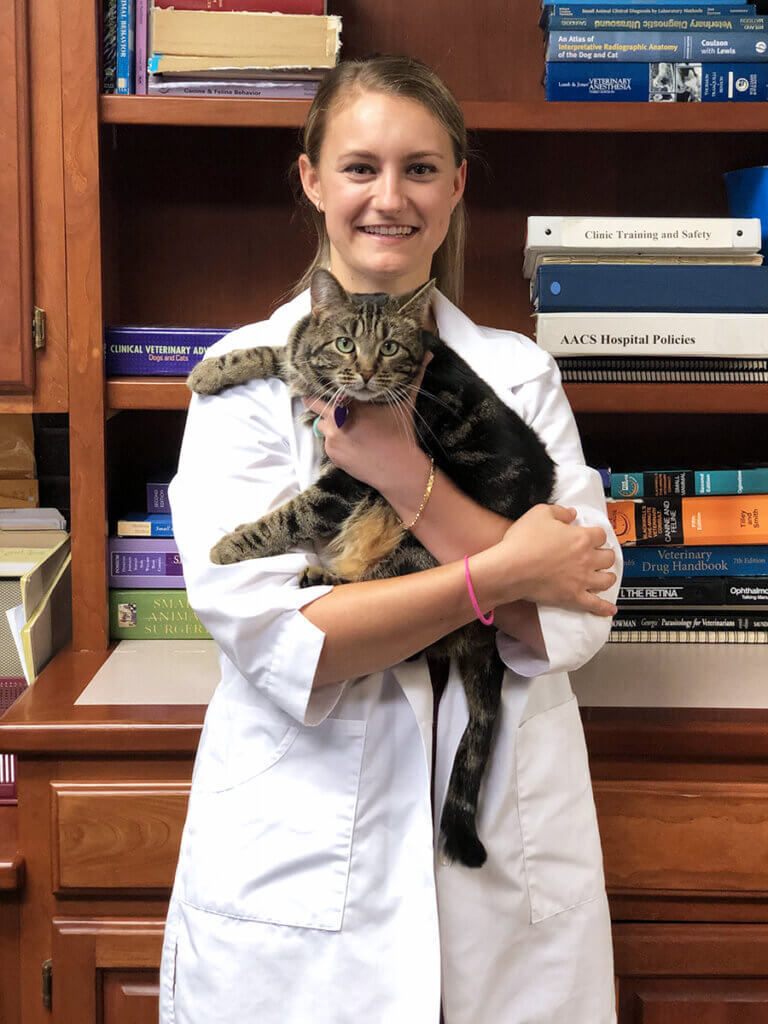 Dr. Ballard wears a white coat holding a tiger stripe cat smiling into the camera