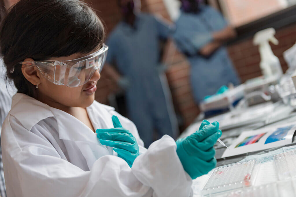 A child in protective eyewear and gloves is conducting a science experiment at a lab table.