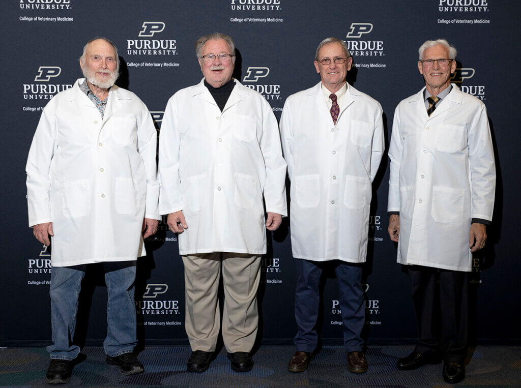 Members of the Class of 1970 don white coats in front of a photo backdrop for a group photo