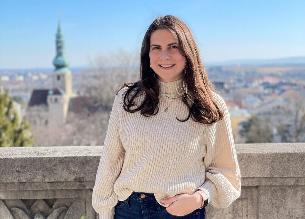 Katelyn stands against a stone wall with the town in the background