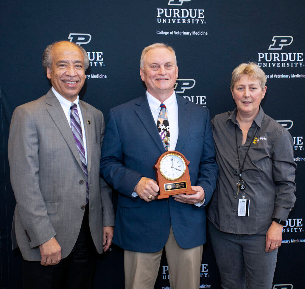 Dr. Baird holds up a clock gift as he is joined by Dean Reed and Dr. Scott Moncrieff