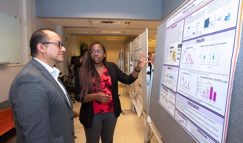 Malaycia speaks gesturing toward a section of her poster as Dr. Munguia smiles listening