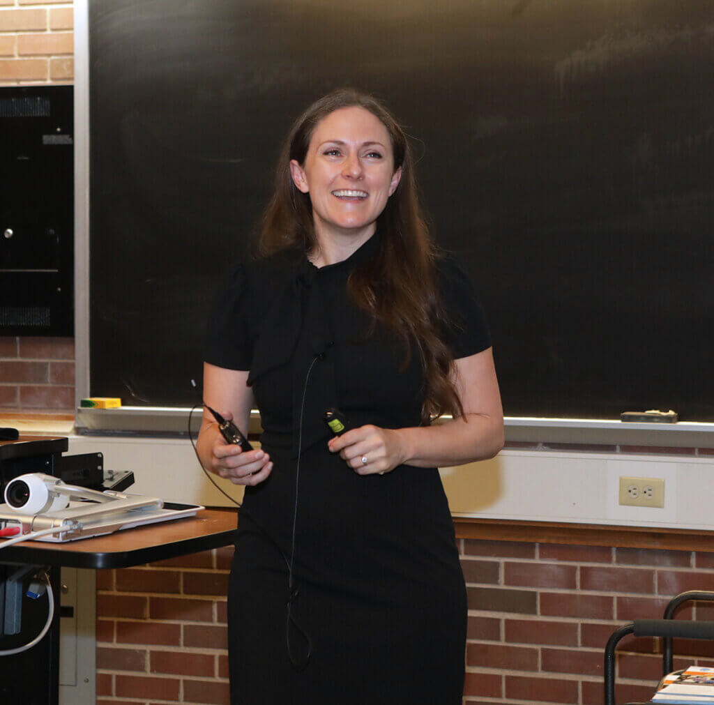 Maggie smiles as she speaks from the front of a lecture room in Lynn Hall