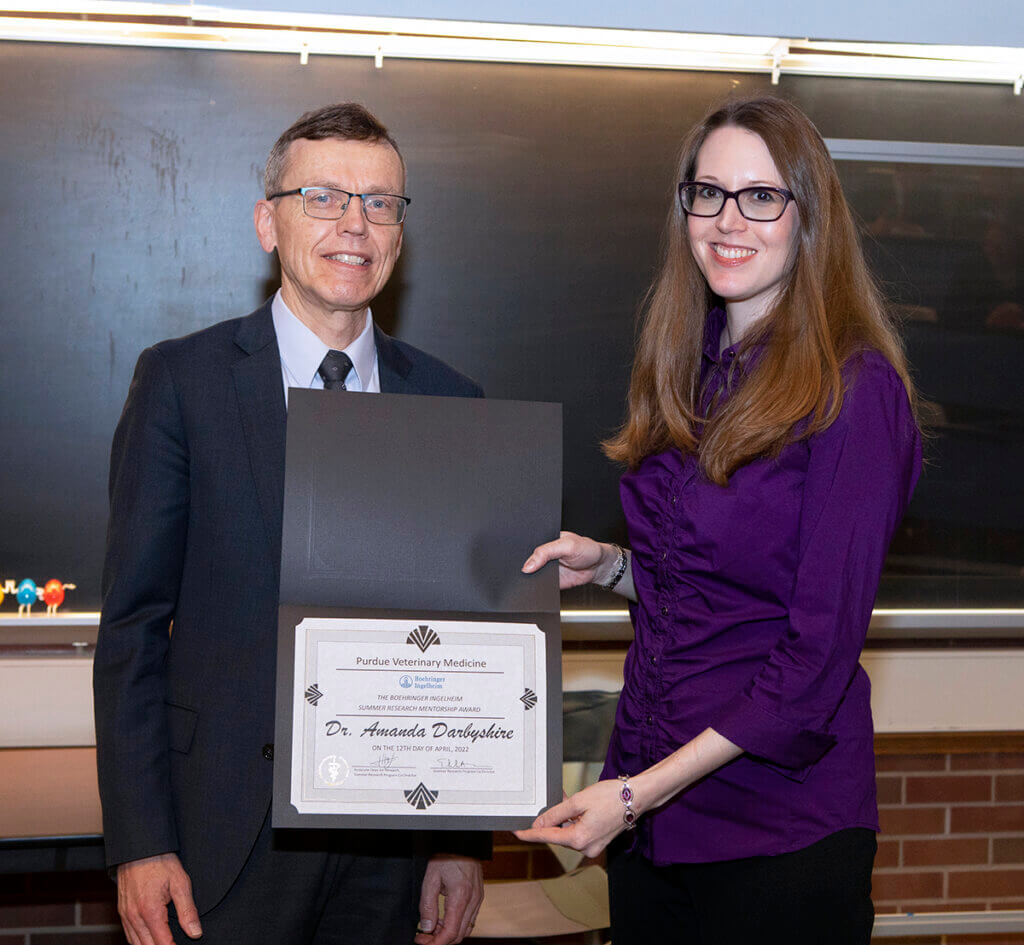 Dr. Darbyshire smiles holding up her award certificate as she is joined by Dr. HogenEsch