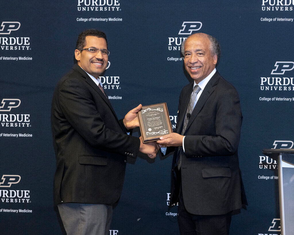 Dr. Sayedahmed and Dean Reed shake hands and hold up his award plaque as they smile into the camera