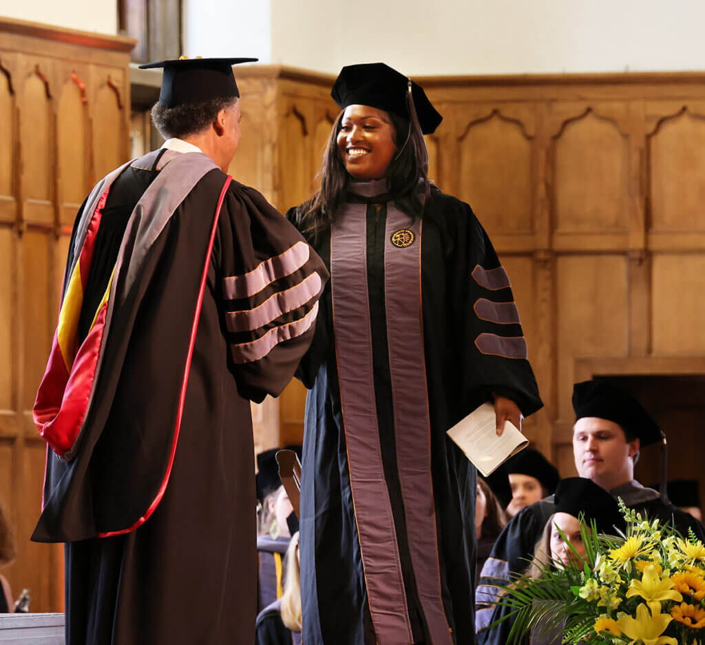 Leah smiles as she shakes hands with Dean Reed as graduates line up behind her to be recognized