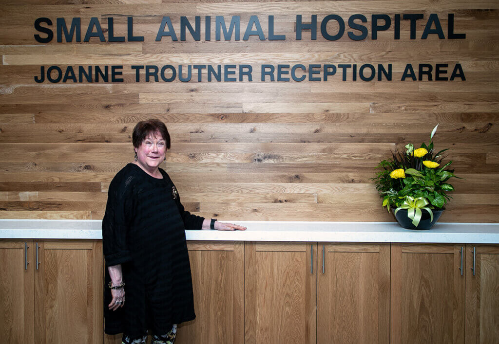 Joanne stands smiling with her hand on the counter of the Joanne Troutner Reception Area of the Small Animal Hospital