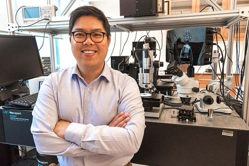 Dr. Lee stands smiling with his arms crossed in his lab