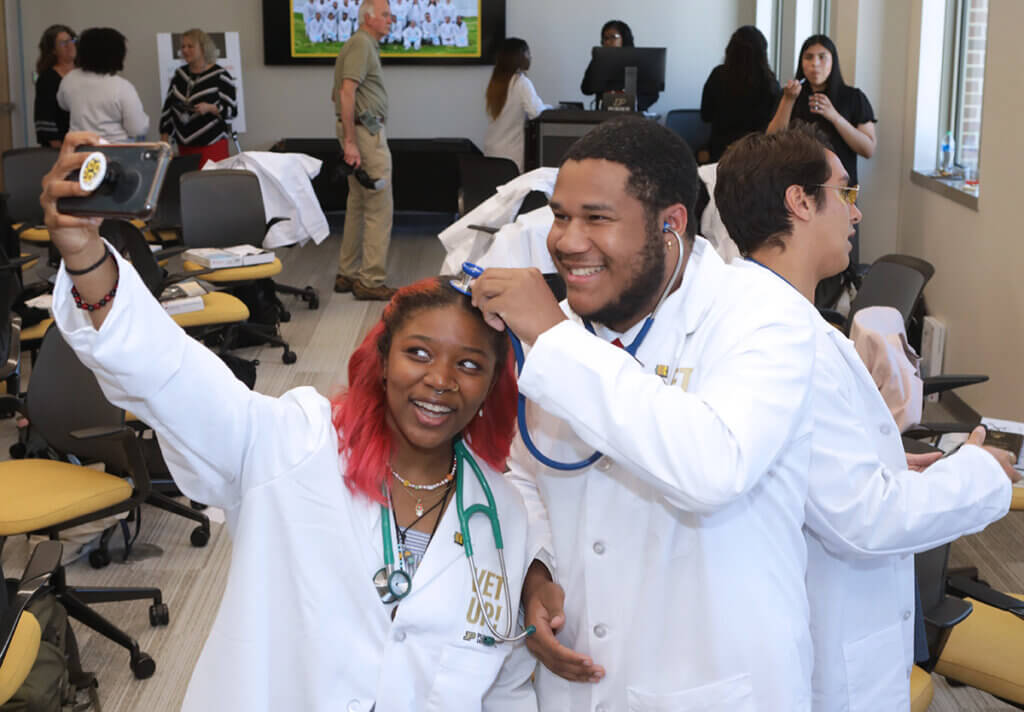 Two participants take a selfie with a stethoscope creatively set on top of one of the participant's head