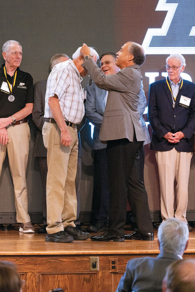 Dean Reed places a medallion over a 50th reunion class member's head as he joins fellow classmates on stage