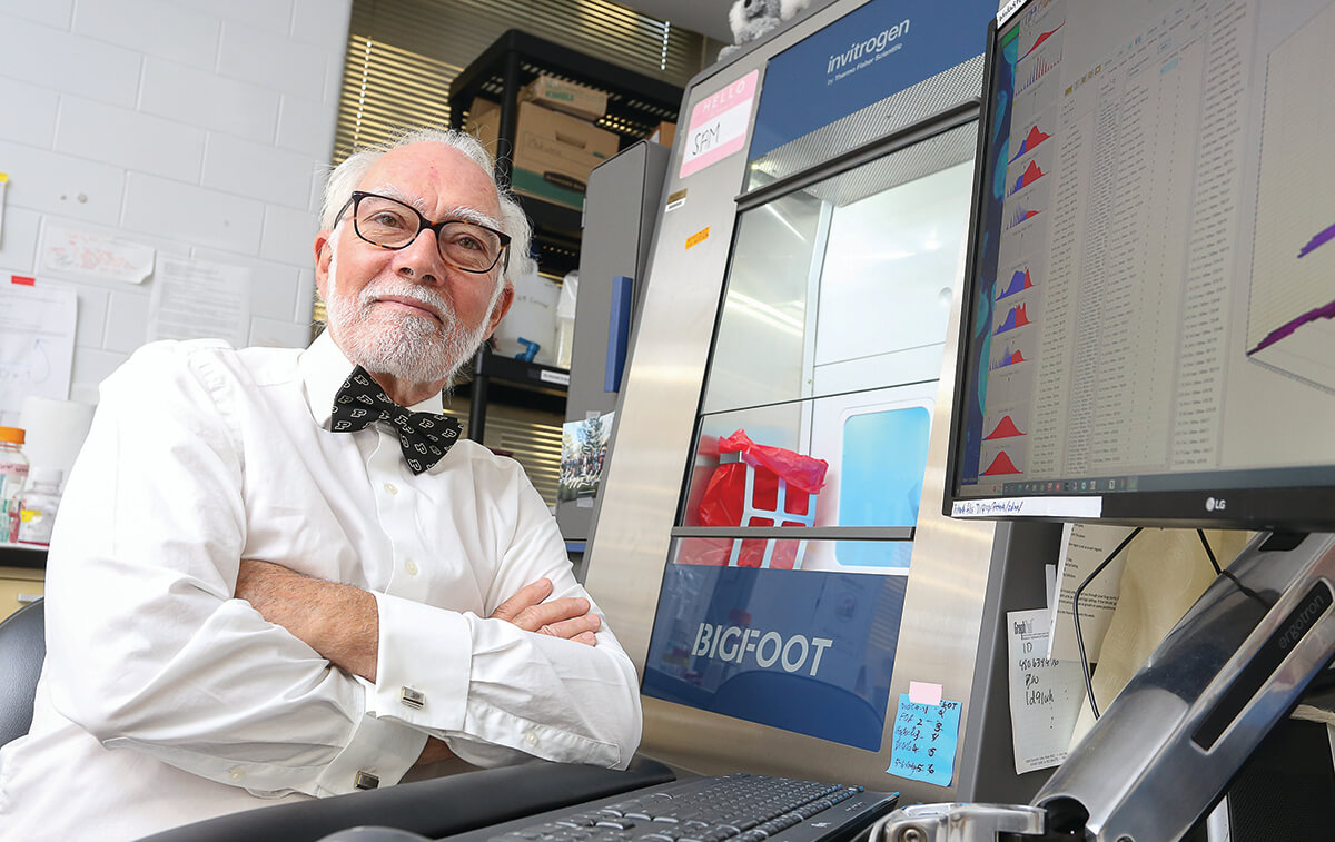 Dr. Robinson sits with his arms crossed in front of him next to the Bigfoot cell sorter and computer monitor