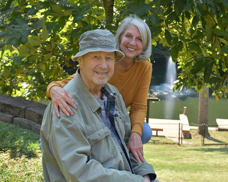 Evan and Sue Ann are pictured smiling sitting outside beneath a shade tree