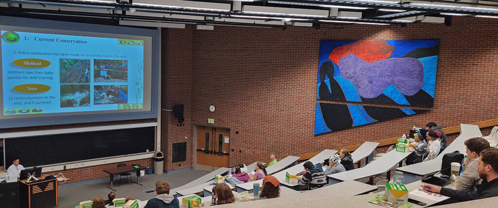 Dr. Wang speaks to the group as his presentation slideshow is displayed above him