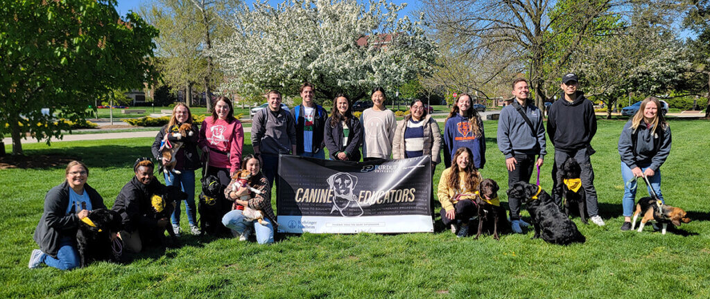Students and pups join for a group photo in front of the Canine Educator banner on Purdue's Memorial Mall