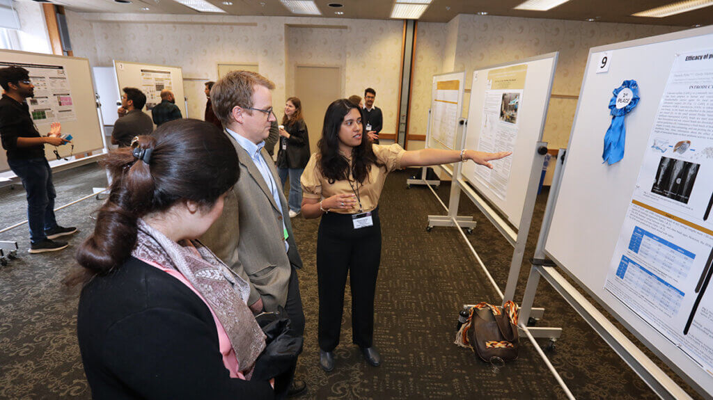 Dr. Hernandez points to her poster as she engages with fellow conference attendees
