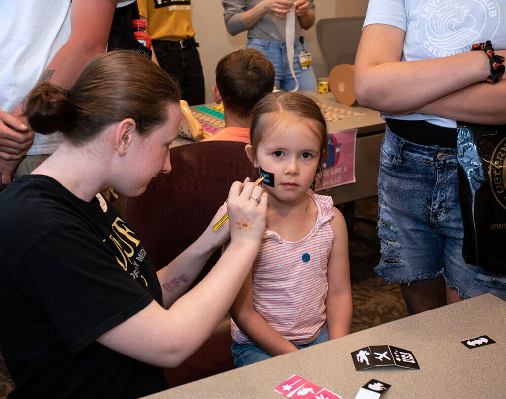 A young girl sits very still as she has her face painting by a Veterinary Nursing student