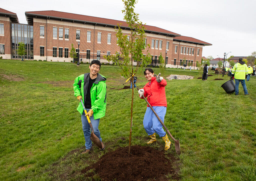 Dr. Malek flashes a peace sign as she and Mu finish planting their tree