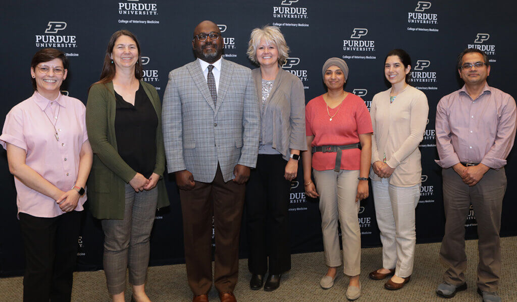 Promoted faculty join together for a group photo against the college's logo backdrop.