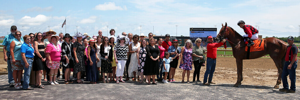 The college's group is joined by the winning horse and his team alongside the horse track