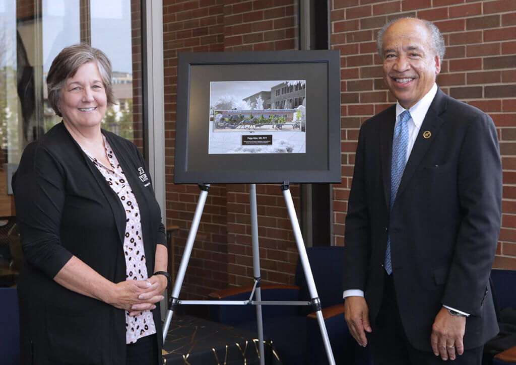 Paige and Dean Reed smile as the stand on either side of her retirement gift displayed on a pedestal in the library