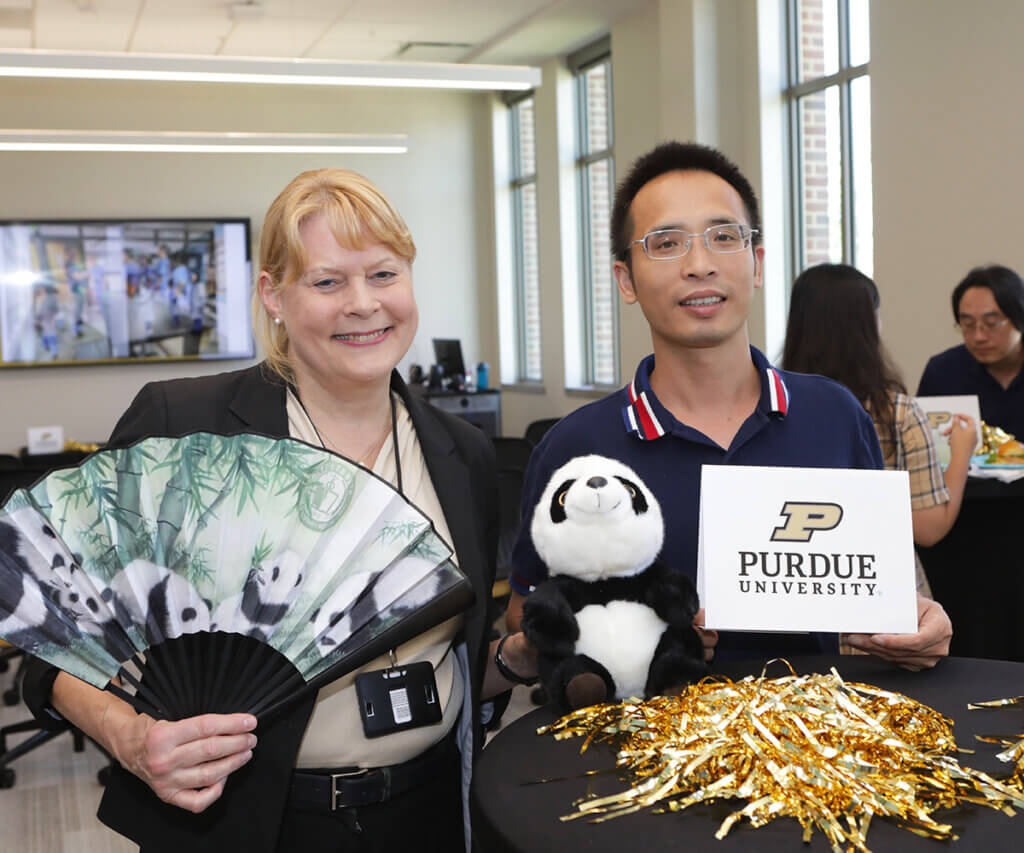 Dr. Salisbury holds up a panda themed paper fan and stuffed panda as she smiles joined by Dr. Zhong at the reception