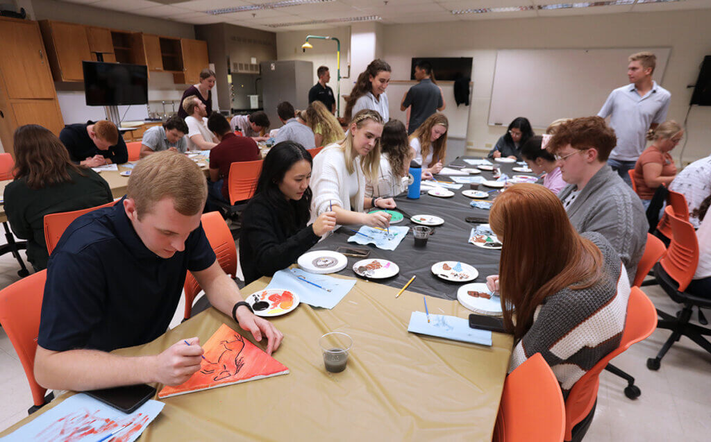 Students are seated painting small canvases in various shapes