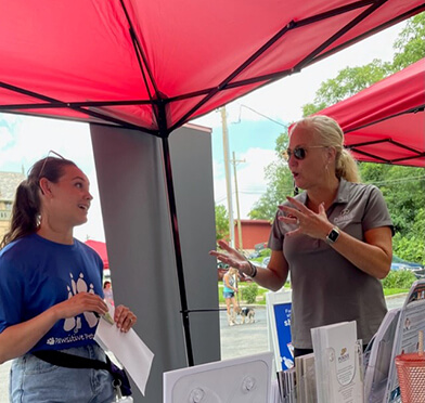 Kelly speaks with an attendee under a red tent awning at the outdoor event