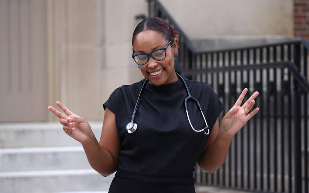 Jadon smiles flashing peace signs with her brand new stethoscope draped around her neck