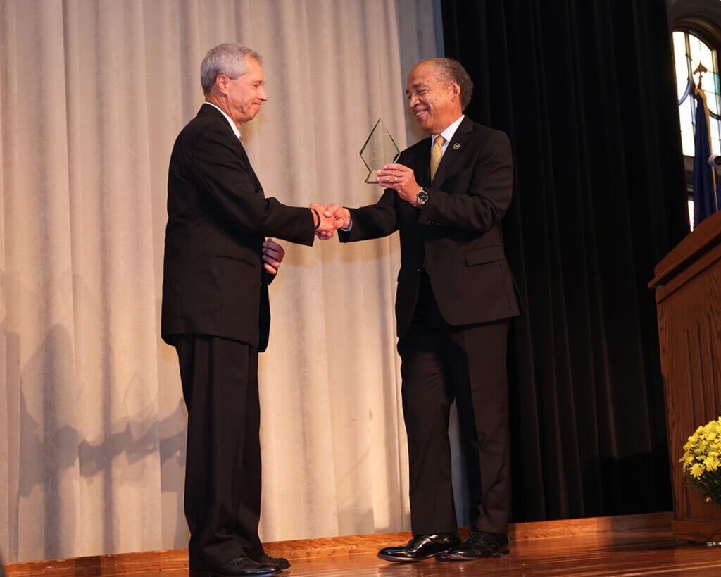 Dr. Hilton receives his award as he shakes Dean Reed's hand on stage.
