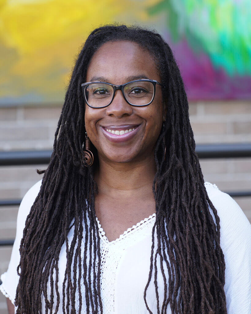 Tia smiles into the camera with a colorful painting on the wall in the background