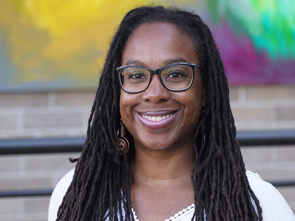 Tia smiles into the camera with a colorful painting on the wall in the background