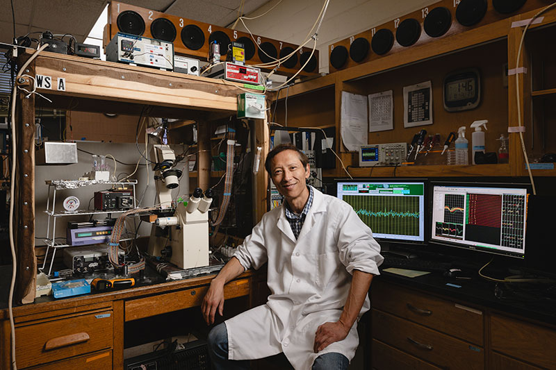 Dr. Shi smiles as he sits in his laboratory surrounded by equipment
