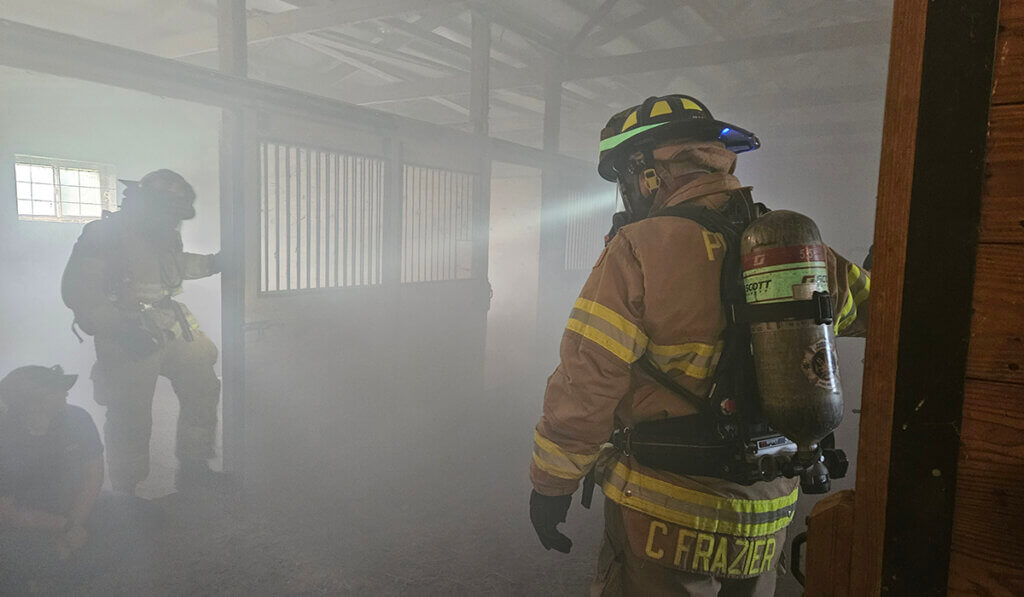 Firefighters walk through a smoke filled barn as a participant sits listening