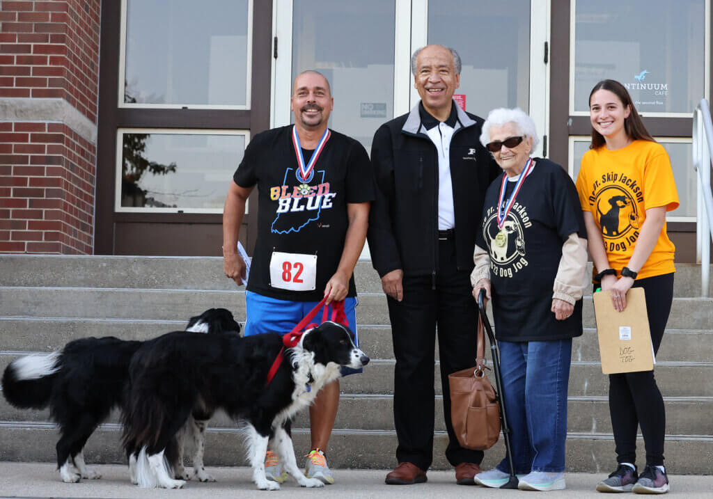 Kevin and his black and white dogs stand alongside Dean Reed, Betty, and Allison on the steps of Lynn Hall to receive his recognition and gift card