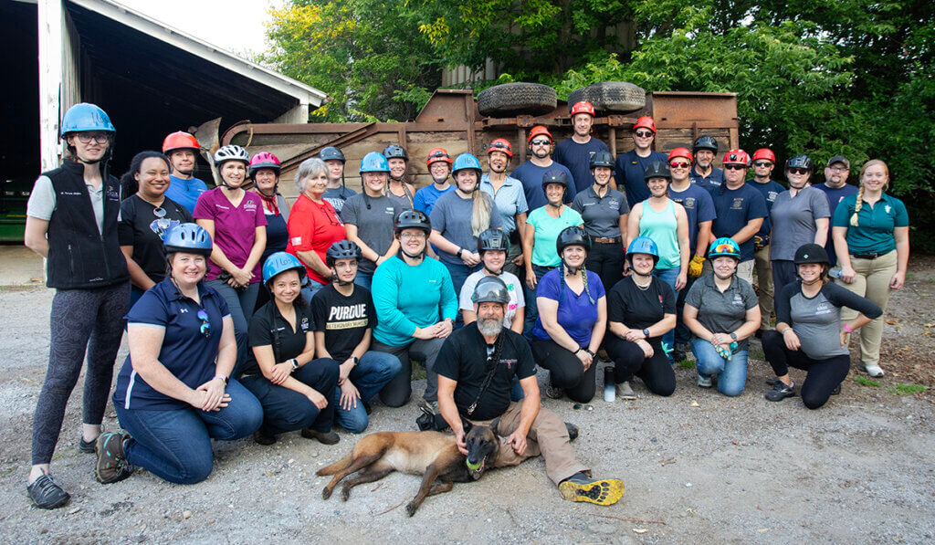 Participants and instructors gather for a group photo along with a pup in front of the overturned trailer