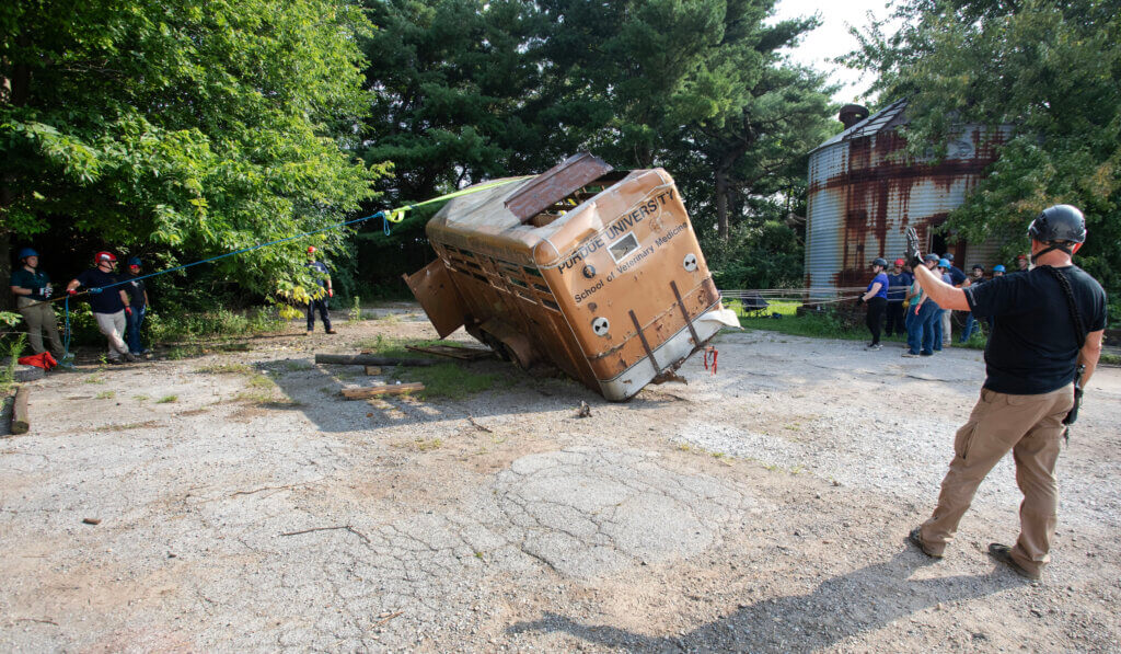 Participants stand on either side of the overturned trailer helping to safely overturn the trailer with ropes and direction from safety personnel