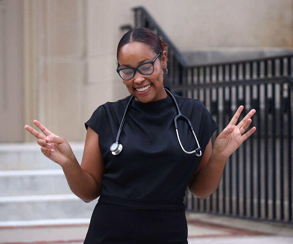Jadon flashes peace signs as she smiles wearing her new stethoscope on the steps of the Union.
