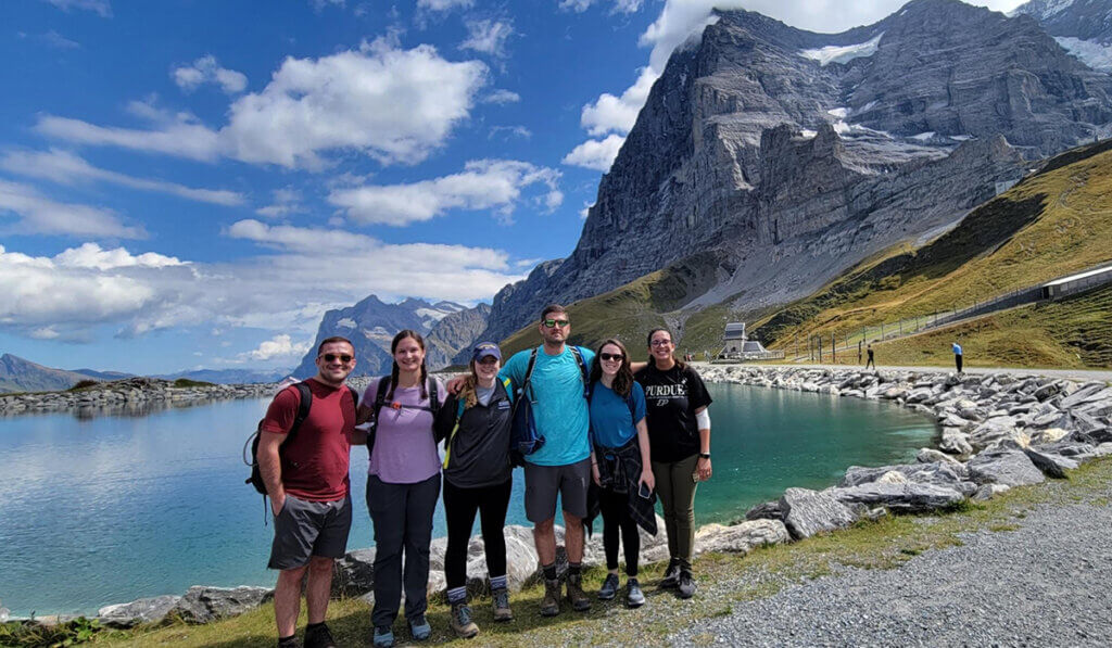 Students take a group photo in front of a picturesque lake and mountain region in Switzerland