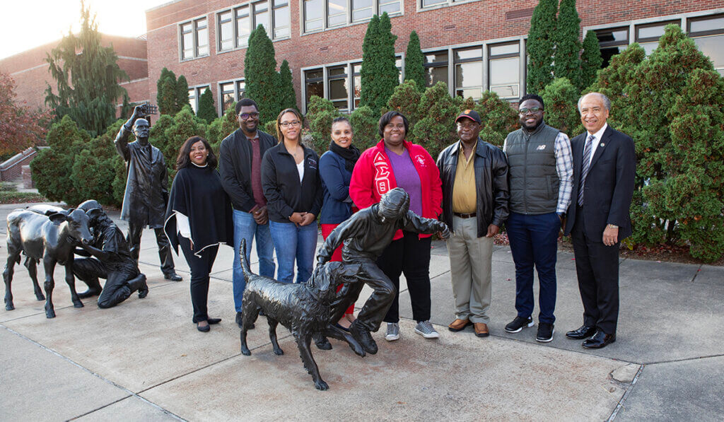 Marsha Baker and Dean Reed join representatives from Vet Up! partner universities for a group photo by the Continuum sculpture in front of Lynn Hall.