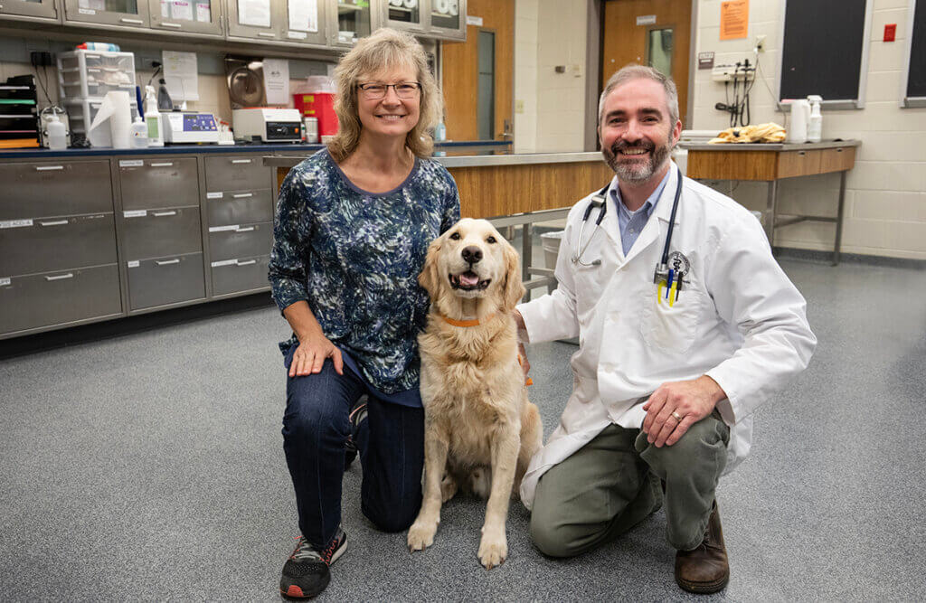 Dr. Childress kneels beside Kody the Golden Retriever and his owner in the oncology treatment room in the Small Animal Hospital